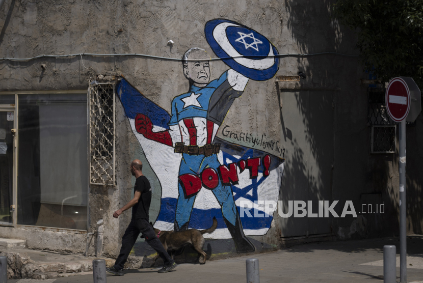 Seorang pria berjalan melewati mural yang menggambarkan presiden AS Joe Biden sebagai pahlawan super yang membela Israel di sebuah jalan di Tel Aviv, Israel, Ahad, 14 April 2024.