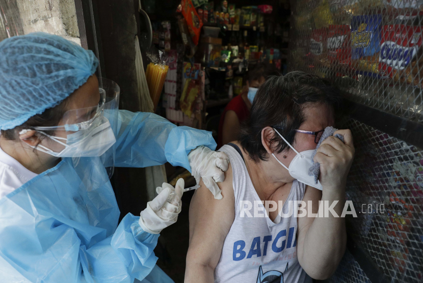 Seorang wanita bereaksi saat petugas kesehatan menyuntiknya dengan vaksin Covid-19 Sinovac China di luar toko mereka di Manila, Filipina pada hari Rabu, 19 Mei 2021.