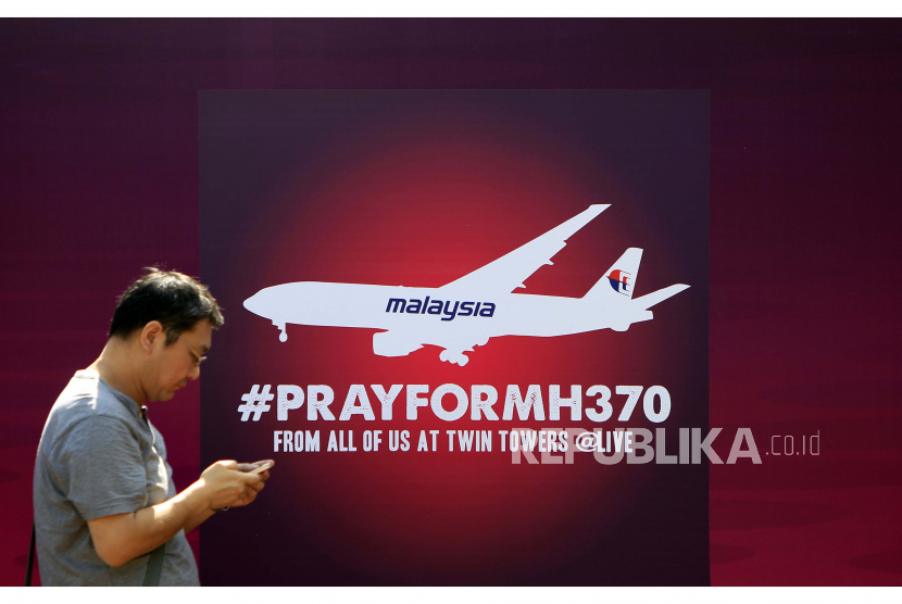 FILE - Seorang pria berjalan melewati papan bertuliskan Doakan MH370 untuk penumpang pesawat Malaysia Airlines yang hilang, di Kuala Lumpur, Malaysia, pada 15 Maret 2014. 