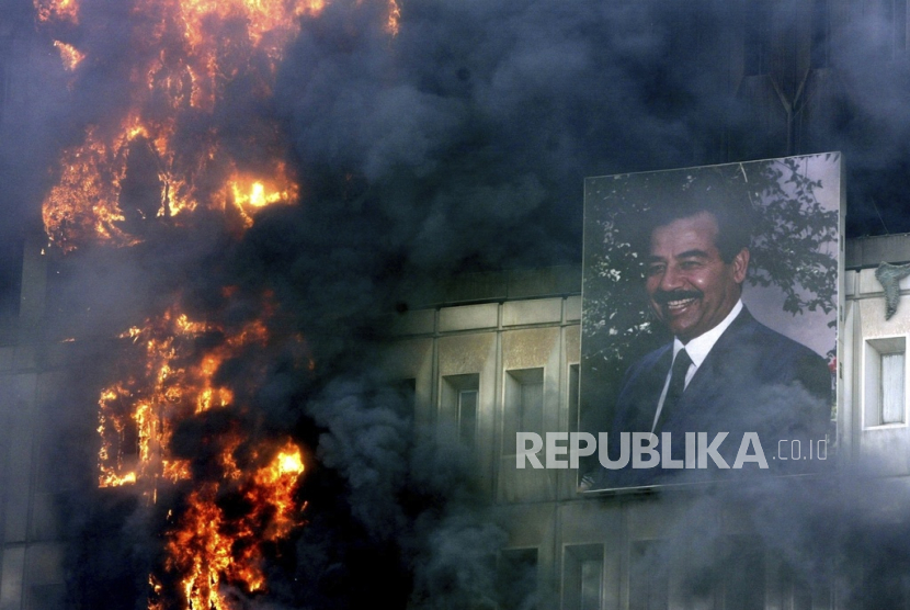  FILE - Potret Saddam Hussein masih tergantung di gedung Kementerian Transportasi dan Komunikasi yang terbakar di Bagdad, 9 April 2003. Ribuan orang mengamuk saat pasukan AS bergerak ke ibu kota Irak.