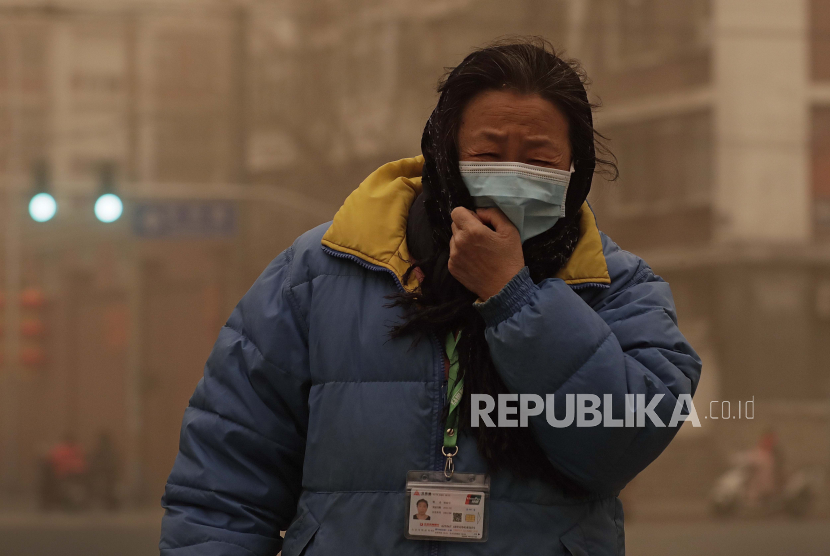 Seorang wanita yang memakai masker wajah bereaksi dari badai pasir saat dia berjalan di seberang jalan di Beijing, Senin, 15 Maret 2021. Ibu kota China, Beijing, untuk pertama kalinya memenuhi standar kualitas udara pada 2021.