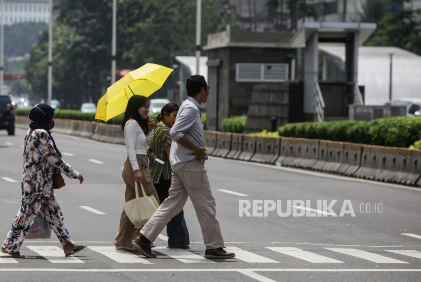 Warga memakai payung saat melintasi Jalan Jenderal Sudirman, Jakarta, Kamis (2/5/2024). 