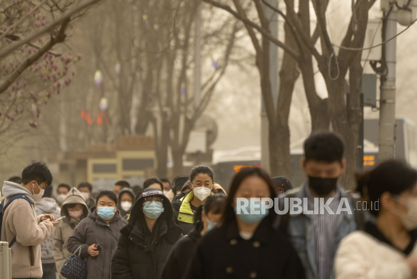 Orang-orang yang memakai masker berjalan di sepanjang jalan di kawasan pusat bisnis di Beijing, 22 Maret 2023. 