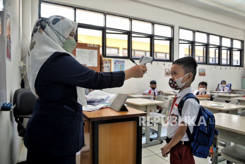 Tenaga pendidik mengecek suhu pelajar usai mengikuti kegiatan Pembelajaran Tatap Muka di SDN 01 Pondok Labu, Jakarta Selatan, Senin (3/1). 