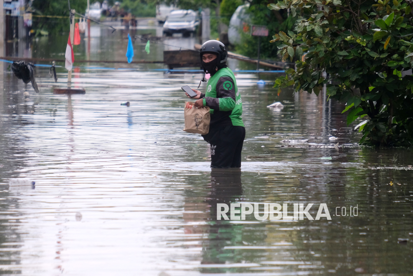 Seorang pengendara ojek daring berjalan melewati banjir untuk mengantar makanan pesanan pelanggan di kawasan Legian, Kuta, Badung, Bali. (ilustrasi)