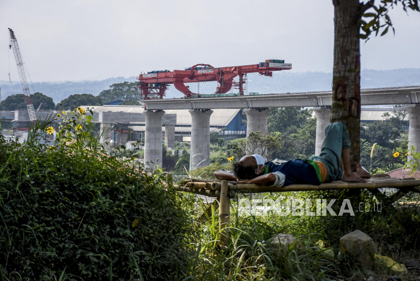 Seorang warga tidur dengan latar belakang proyek konstruksi Kereta Cepat Jakarta-Bandung (KCJB) di Lembah Teratai, Desa Gadobangkong, Kecamatan Ngamprah, Kabupaten Bandung Barat, Ahad (8/8). 