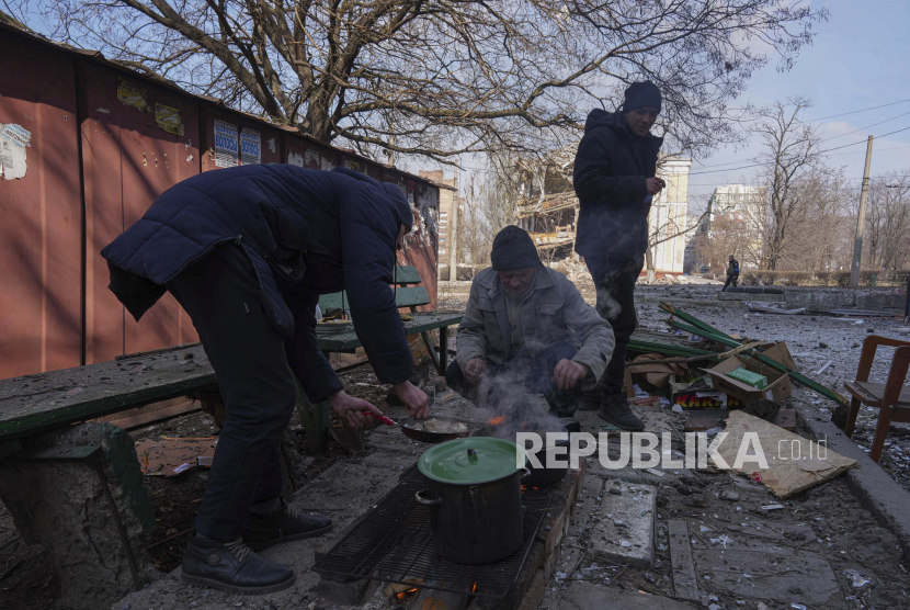 Para pria memasak makanan di sebuah jalan di Mariupol, Ukraina, Ahad, 13 Maret 2022. Rusia menyerukan pasukan Ukraina yang terlibat pertempuran di kota Mariupol untuk meletakkan senjata.  