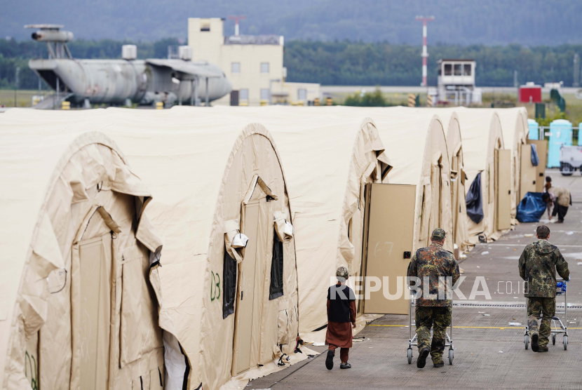Pengungsi Afghanistan di Prancis Kesulitan Bawa Keluarga. Foto: Tentara AS berjalan melewati deretan tenda dan seorang pengungsi muda Afghanistan, di Pangkalan Udara Ramstein, di Ramstein-Miesenbach, Jerman, Senin, 30 Agustus 2021. 