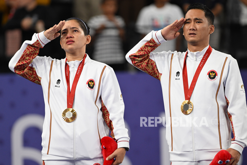 Pebulu tangkis ganda campuran Indonesia Leani Ratri Oktila (kiri) bersama rekannya, Hikmat Ramdani (kanan) melakukan penghormatan kepada bendera Merah Putih usai upacara pengalungan medali bulu tangkis ganda campuran SL3-SU5 Paralimpiade 2024 Paris di Porte de la Chapelle Arena, Paris, Prancis, Senin (2/9/2024). Hikmaat dan Ratri menang dengan skor 21-16, 21-15 atas lawan senegaranya, Fredy Setiawan dan Khalimatus Sadiyah sekaligus memastikan diri meraih medali emas, sementara Fredy dan Khalimtus meraih medali perak. 