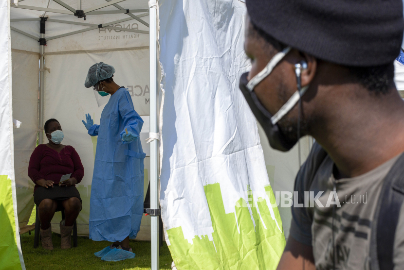 Seorang pria melihat melalui celah tenda ketika seorang wanita menyaksikan pekerja kesehatan menjelaskan proses mengumpulkan sampel untuk pengujian virus corona, selama kampanye penyaringan dan pengujian yang bertujuan untuk memerangi penyebaran COVID-19 Diepsloot, utara di Johannesburg, Afrika Selatan, Jumat, 8 Mei 2020.