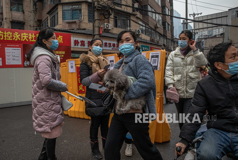  Seorang wanita yang mengenakan masker pelindung wajah dengan seekor anjing berjalan melewati sukarelawan keamanan publik yang berdiri di samping pagar keamanan dan memeriksa kode kesehatan orang-orang untuk mencegah penyebaran penyakit virus corona (Covid-19), di daerah pemukiman di Wuhan, Cina, 22 Januari 2021. 