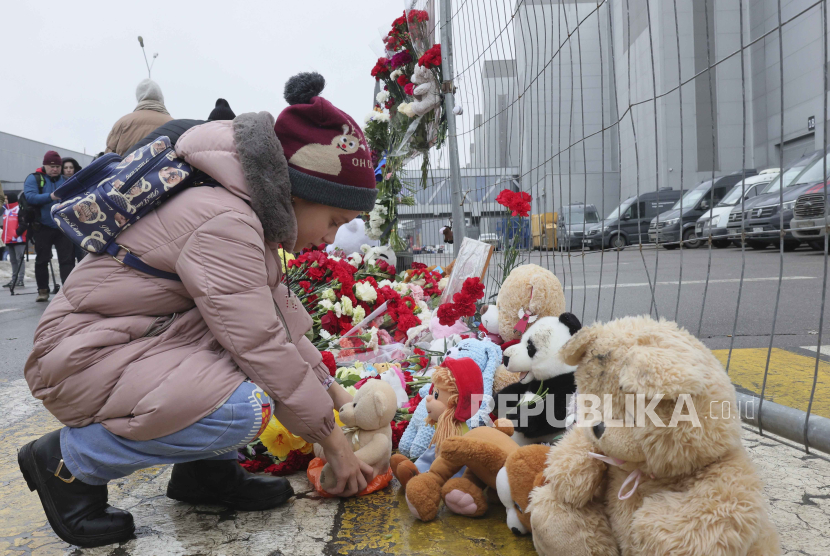 Seorang anak meletakkan mainan di pagar sebelah Balai Kota Crocus, di tepi barat Moskow, Rusia, Sabtu, (23/3/2024). 