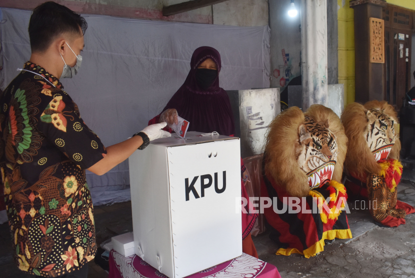 Petugas Kelompok Penyelenggara Pemungutan Suara (KPPS) memandu pemilih memasukkan surat suara ke kotak suara di sebuah TPS (ilustrasi).