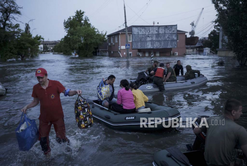 Seorang pekerja darurat membawa barang-barang warga yang dievakuasi dari lingkungan yang terkena banjir di Kherson, Ukraina, Selasa, (6/6/2023).