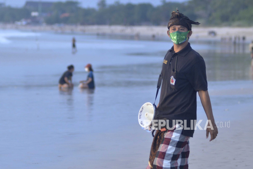Pecalang atau petugas keamanan adat Bali melakukan pengawasan penerapan protokol kesehatan terhadap pengunjung Pantai Jimbaran di Badung, Bali, Jumat (10/7/2020).