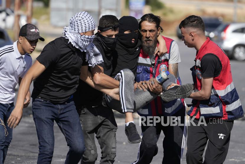  Warga Palestina menggendong seorang pria yang terluka dalam bentrokan dengan tentara Israel setelah unjuk rasa memperingati 74 tahun apa yang disebut warga Palestina sebagai Nakba, atau malapetaka yang mengacu pada keterpurukan mereka dalam perang atas pembentukan Israel tahun 1948, di kota Ramallah, Tepi Barat, Ahad. 15 Mei 2022.