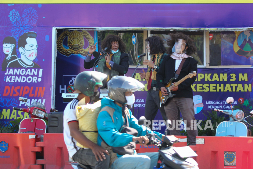 Polisi berpakaian sipil bermain musik saat  sosialisasi penerapan protokol kesehatan di depan pos pengamanan di Surabaya, Jawa Timur, Rabu (23/12/2020). Sosialisasi dengan menyisipkan protokol kesehatan yaitu Memakai Masker, Menjaga Jarak, Mencuci Tangan dalam lagu yang dinyanyikannya itu bertujuan agar masyarakat tetap terus menerapkan protokol kesehatan pencegahan penyebaran COVID-19 dalam kesehariannya. 