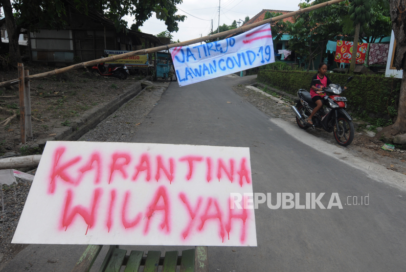 Warga melintas di dekat portal karantina wilayah di Sawit, Boyolali, Jawa Tengah, Selasa (31/3/2020). Pelemahan ekonomi yang merupakan dampak dari pembatasan atas covid-19 dikhawatirkan akan meningkatkan kriminalitas. 