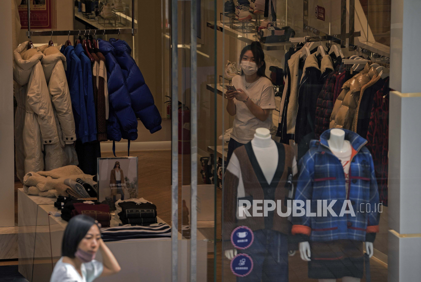 Seorang wanita dengan masker wajah di dagunya berjalan di dekat toko pakaian.