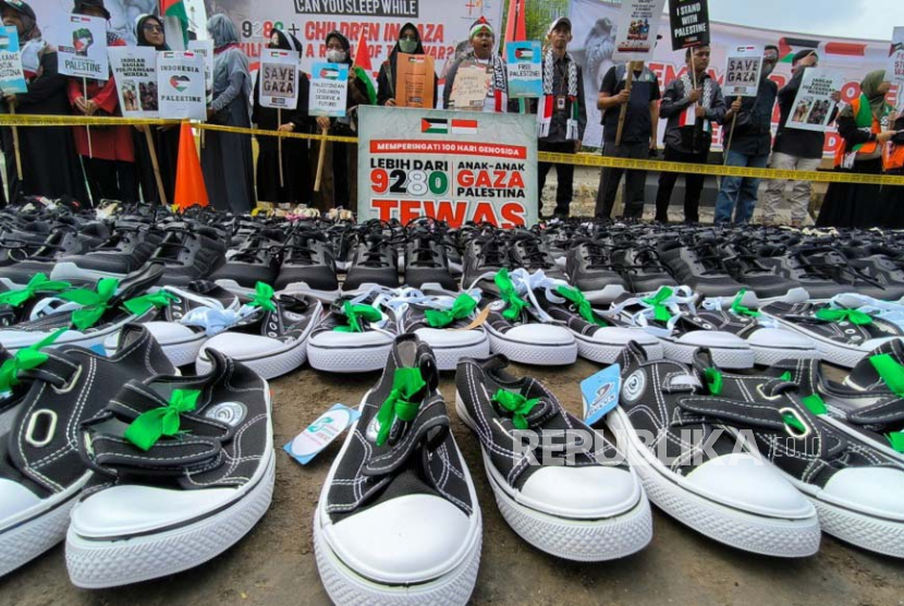 Aktivis Muslim memegang poster dan memajang ratusan sepatu anak-anak saat unjuk rasa Pro-Palestina yang diadakan untuk memperingati 100 hari perang di Gaza, di depan kedutaan AS di Jakarta, Senin, (15/1/2024).