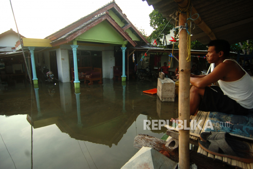 Seorang warga duduk di depan rumahnya yang tergenang air rob (banjir pasang air laut) 
