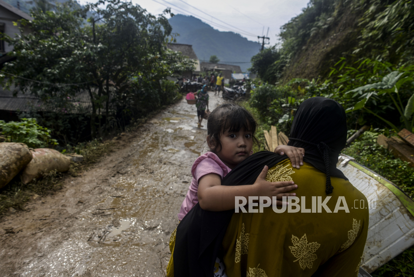 Seorang anak digendong orang tuanya melintasi jalan yang tertutup lumpur di Desa Purasari, Leuwiliang, Kabupaten Bogor, Jawa Barat, Kamis (23/6/2022). BPBD menargetkan tiga bulan investigasi banjir bandang Pamijahan-Leuwiliang, Bogor.