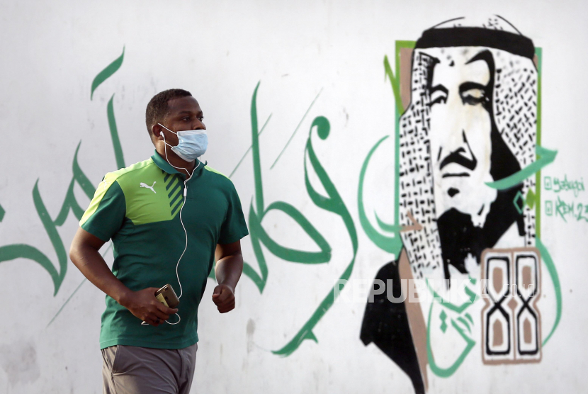 Pekerja Publik Saudi Kembali Bekerja ke Kantor. Foto ilustrasi: Seorang pria memakai masker saat melewati mural Raja Salman di Saudi Arabia, Ahad (28/6). Kasus COVID-19 di dunia mencatatkan angka tertinggi dalam 24 jam terakhir pada Ahad (28/6),  dengan jumlah lebih dari 10 juta kasus positif dan 500.000 kematian. (AP Photo/Amr Nabil)