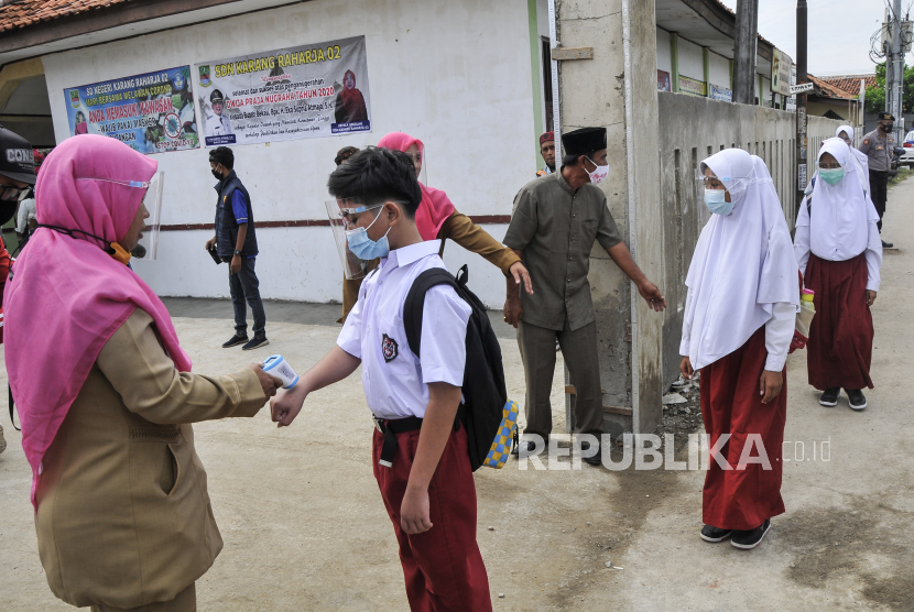 Seorang guru mengukur suhu tubuh muridnya sebelum memasuki simulasi Kegiatan Belajar Mengajar (KBM) tatap muka di SDN Karang Raharja 02 saat simulasi di Cikarang, Kabupaten Bekasi, Jawa Barat.