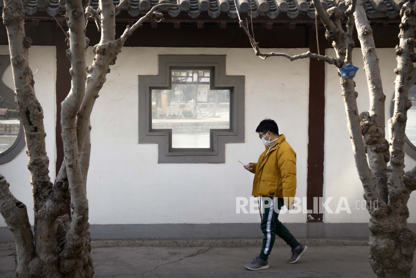  Seorang pria yang mengenakan masker wajah untuk melindungi diri dari COVID-19 melihat smartphone-nya saat dia berjalan di taman umum di Beijing, Rabu, 5 Januari 2022. China melaporkan penurunan besar dalam infeksi COVID-19 lokal di kota utara Xi