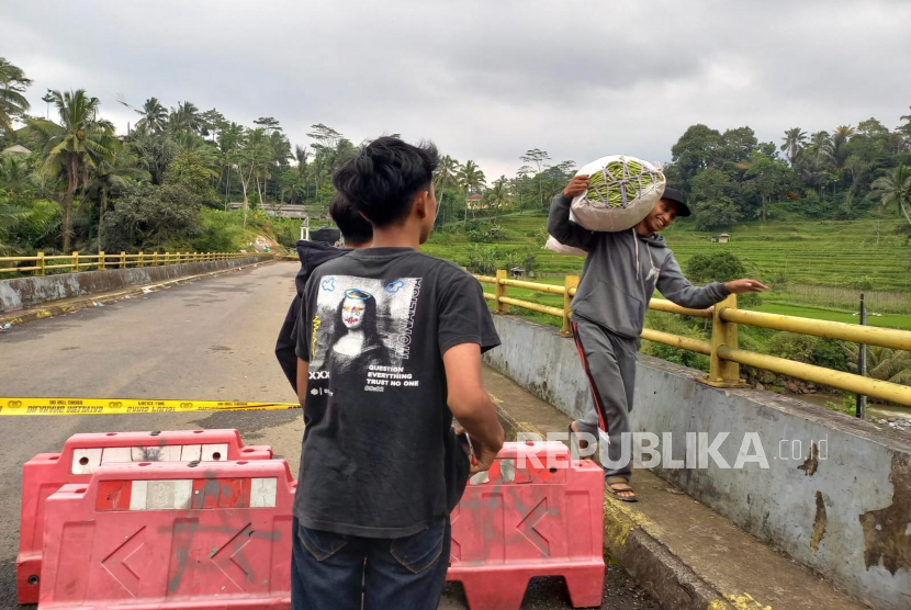 Warga memanggul hasil pertanian melintasi Jembatan Cidugaleun di Kecamatan Cigalontang, Kabupaten Tasikmalaya, Senin (9/5/2023). 