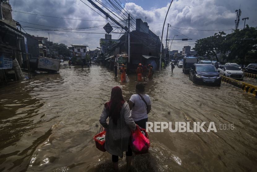 Warga melintasi genangan air saat terjadi banjir di Jalan Jatinegara Barat, Jakarta Timur, Senin (8/2).