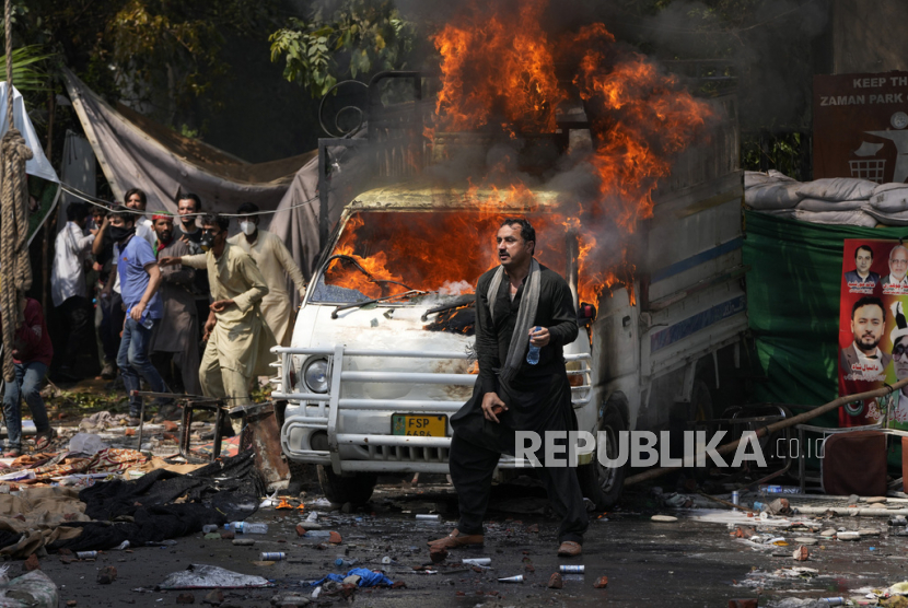  Pendukung mantan Perdana Menteri Imran Khan melemparkan batu ke arah polisi di sebelah kendaraan yang terbakar saat bentrokan, di Lahore, Pakistan, Rabu (15/3/2023). Imran Khan secara resmi menandai kehadirannya di pengadilan di Islamabad pada Sabtu (18/3/2023).