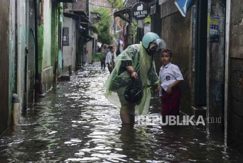 Seorang anak bersama orang tuanya saat akan berjalan melewati banjir. (Ilustrasi)