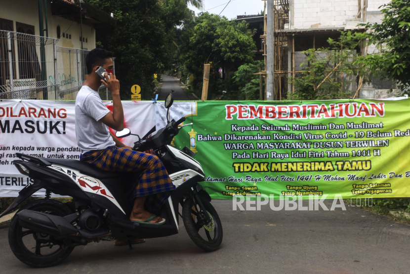 Warga berada di pintu masuk kampung yang ditutup di Terwilen, Margodadi, Seyegan, Sleman, Daerah Istimewa Yogyakarta (DIY).