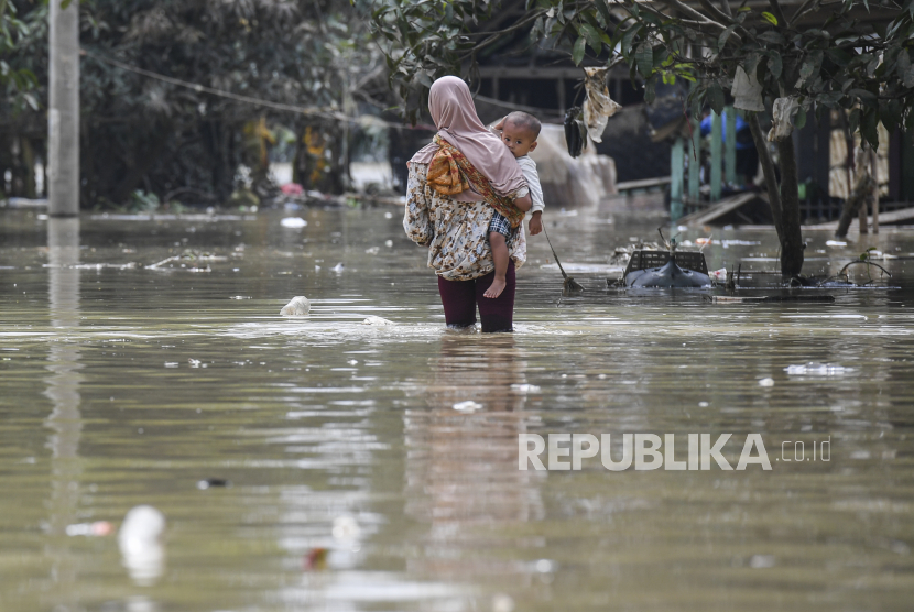 Hukum Meratapi Musibah Berlebihan dan Menyalahkan Allah? Seorang ibu menggendong anaknya melintasi pemukiman yang masih terendam banjir di Karangligar, Telukjambe Barat, Karawang, Jawa Barat, Kamis (25/2/2021).