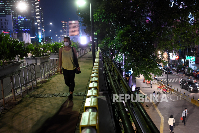 Seorang warga yang mengenakan masker berjalan di trotoar jalan MH Thamrin Jakarta, Kamis (1/10). Pengendalian penanganan Covid-19 terus menunjukkan perbaikan. Hal ini terlihat dari tingkat positif atau positivity rate Covid-19 harian yang trennya menurun. 