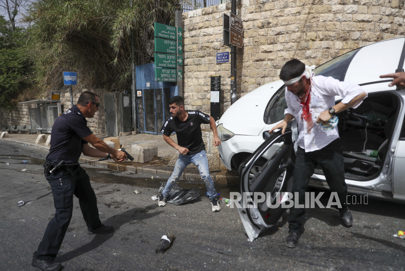  Palestina Israel: Seorang petugas polisi Israel berdiri dengan pistol menunjuk ke arah seorang pria Palestina, di tengah, di samping seorang pengemudi Yahudi yang diserang oleh pengunjuk rasa Palestina di dekat Kota Tua Yerusalem, Senin, 10 Mei 2021. 