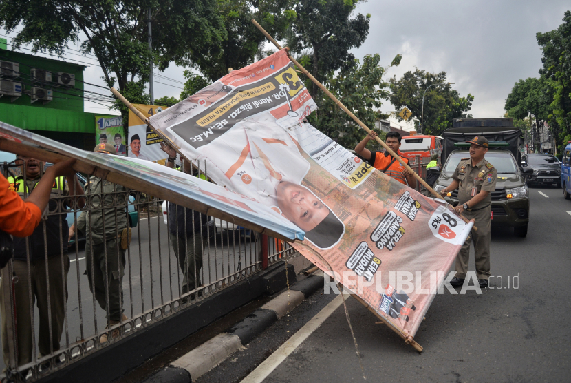 Petugas Satpol PP menertibkan alat peraga kampanye (APK) yang  berada di pembatas jalan di Jalan Raya Bogor, Kramat Jati, Jakarta