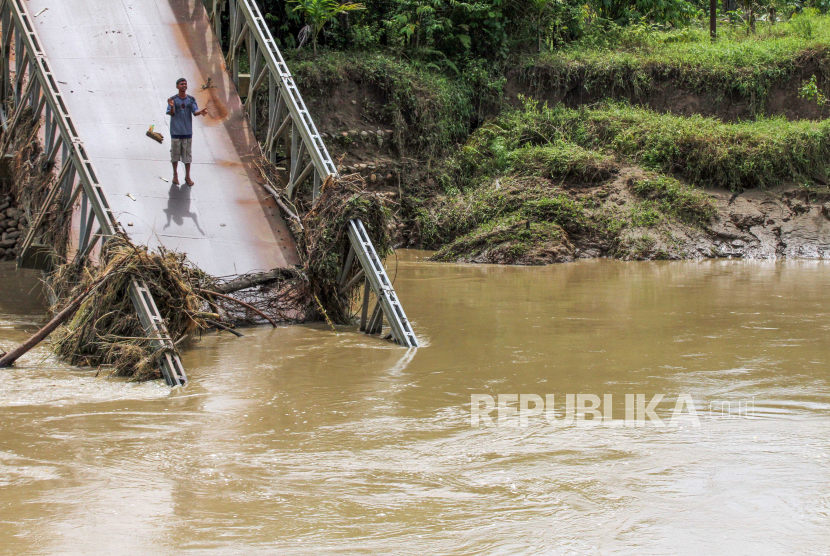 Seorang warga berkomunikasi jarak jauh dari jembatan penghubung yang putus pasca diterjang banjir susulan di Desa Darussalam, Kecamatan Geureudong Pase, Aceh Utara, Aceh, Ahad (13/12/2020). Jembatan bailey penghubung antar desa dan kecamatan itu putus akibat diterjang banjir susulan pada Sabtu (12/12)  yang kembali merendam lima kecamatan di Aceh Utara. 