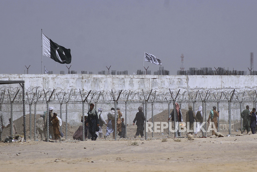 Bendera Pakistan dan Taliban berkibar di sisi masing-masing sementara orang-orang berjalan melalui penghalang keamanan untuk melintasi perbatasan di titik penyeberangan perbatasan antara Pakistan dan Afghanistan, di Chaman, Pakistan, Rabu, 18 Agustus 2021.