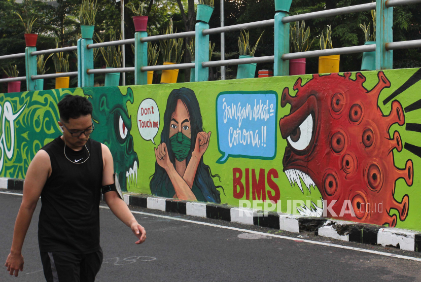 Warga berjalan di dekat dinding bermural di Surabaya, Jawa Timur, Ahad (18/7/2021). Mural tersebut merupakan sarana imbauan kepada warga untuk tetap menerapkan protokol kesehatan pencegahan penularan COVID-19 dalam kesehariannya. 