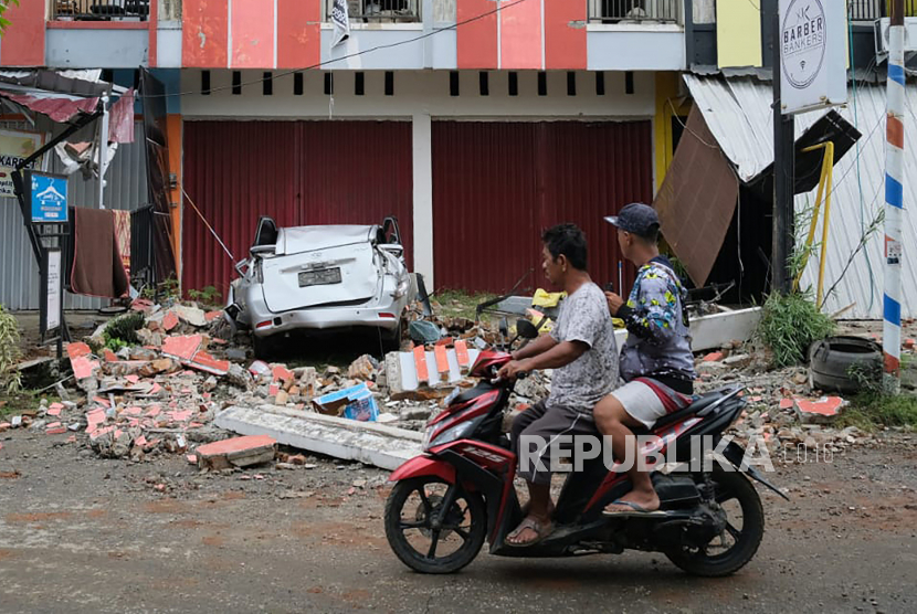  Pengendara kendaraan melewati reruntuhan mobil yang rusak akibat gempa bumi di Mamuju, Sulawesi Barat,  Jumat (15/1/2021). 