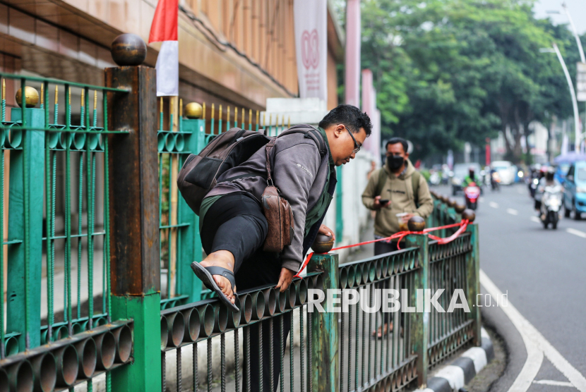 Warga melompati pagar saat berlangsungnya proyek peninggian pagar di Stasiun Cikini, Jakarta Pusat, Selasa (12/8/2025).
