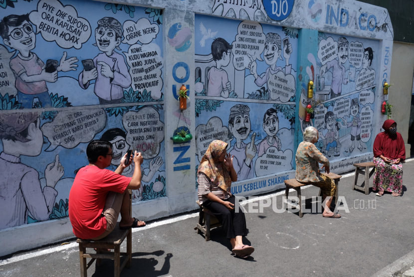 Warga berjemur dengan latar belakang mural (lukisan dinding) komik antihoaks di Kampung Hepi, Joho, Manahan, Solo, Jawa Tengah. (ilustrasi)