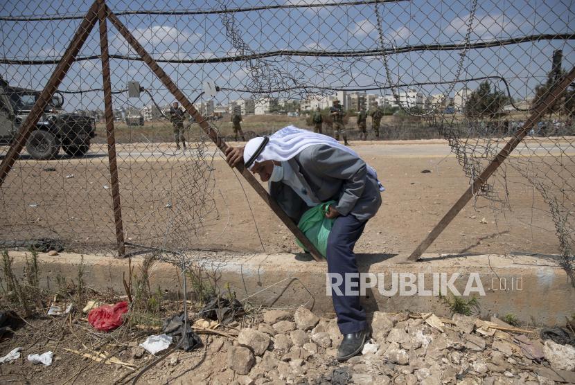  Tentara Israel menyaksikan seorang pekerja Palestina melintasi bagian pagar pemisah Israel yang rusak, pulang ke rumah setelah seharian bekerja di Israel, di desa Jalameh Tepi Barat, dekat Jenin, Senin, 6 September 2021. Generasi muda Palestina kesulitan mendapatkan pekerjaan.