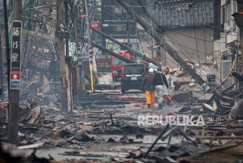 Orang-orang berjalan di tengah sisa-sisa bangunan yang terbakar akibat kebakaran yang terjadi setelah gempa bumi kuat di Wajima, Jepang tengah,  Rabu, (3/1/2024).