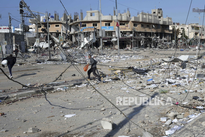 Warga Palestina berjalan di sekitar reruntuhan gedung di Gaza.