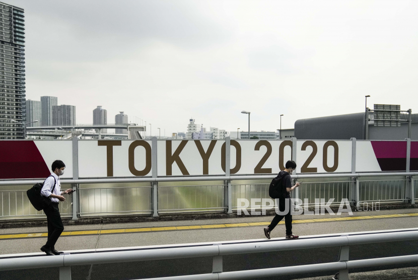  Dua pria berjalan di sepanjang jembatan melewati spanduk Tokyo 2020 menjelang Olimpiade Musim Panas 2020, Selasa, 13 Juli 2021, di Tokyo.