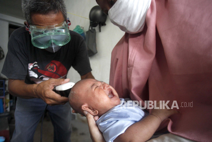 Tukang cukur keliling memakai alat pelindung diri saat memotong rambut bayi di halaman rumah pelanggan, Cimanggis, Depok, Jawa Barat, Rabu (10/6/2020). Balita perlu dikondisikan sebelum cukuran.