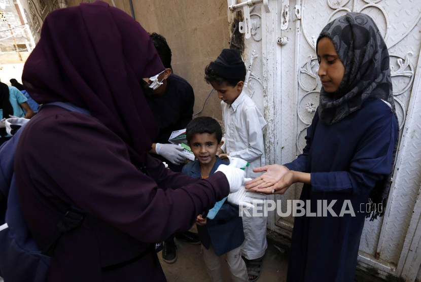 Seorang relawan (kiri) menyemprotkan disinfektan ke tangan anak-anak pada kegiatan pensterilan daerah kumuh dari penyebaran virus Corona (COVID-19) di Sanaa, Yaman, Senin (30/3). Relawan Yaman berinisiatif untuk mensterilkan daerah kumuh di Sanaa dan membantu orang kurang mampu untuk melindungi diri mereka sendiri dan meningkatkan kesadaran mereka tentang SARS-CoV-2 virus Corona yang menyebabkan penyakit COVID-19